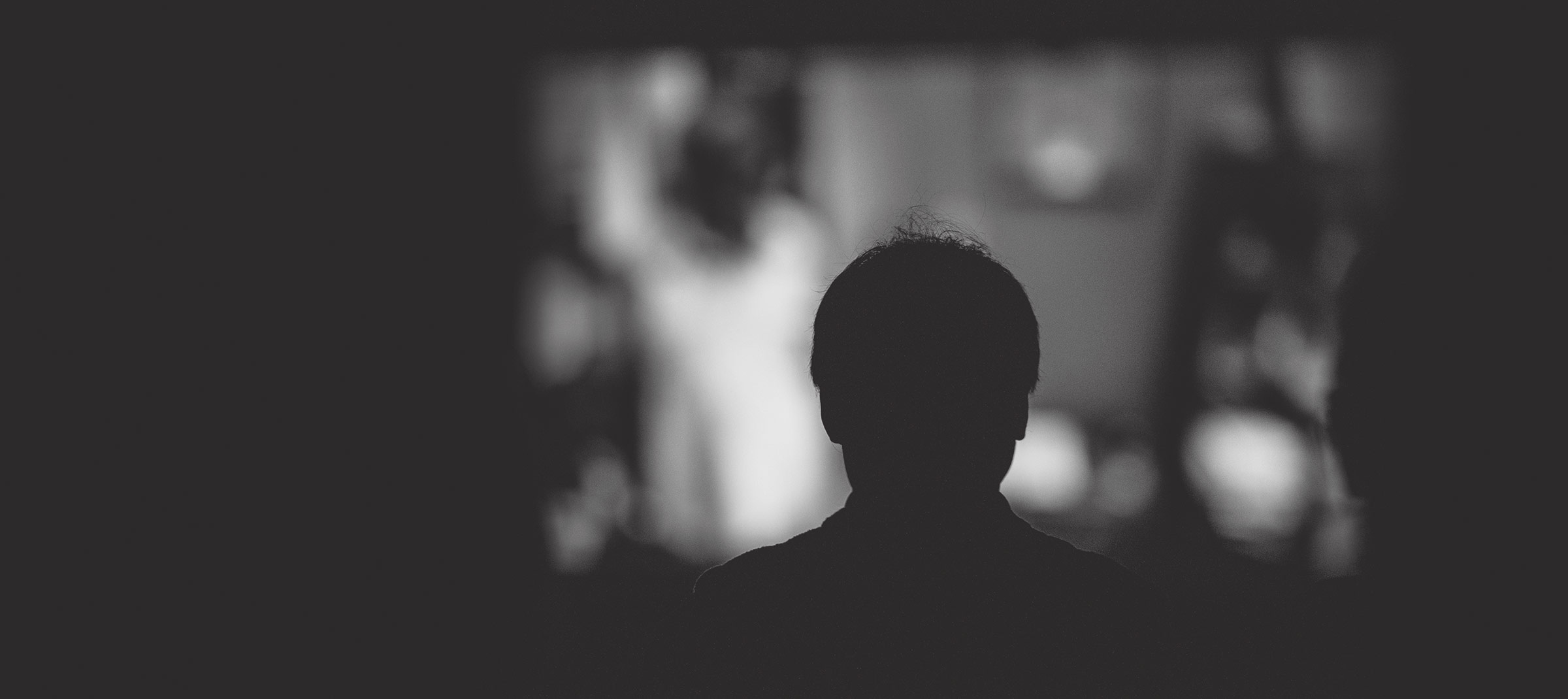 Silhouette of a man watching a film from behind, with out-of-focus screen in the background