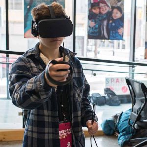 A young person wearing a virtual reality headset, holding hand-held controllers at the ReFrame VR Hub