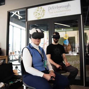 Two individuals, one older and one younger, seated wearing virtual reality headsets at the ReFrame VR Hub