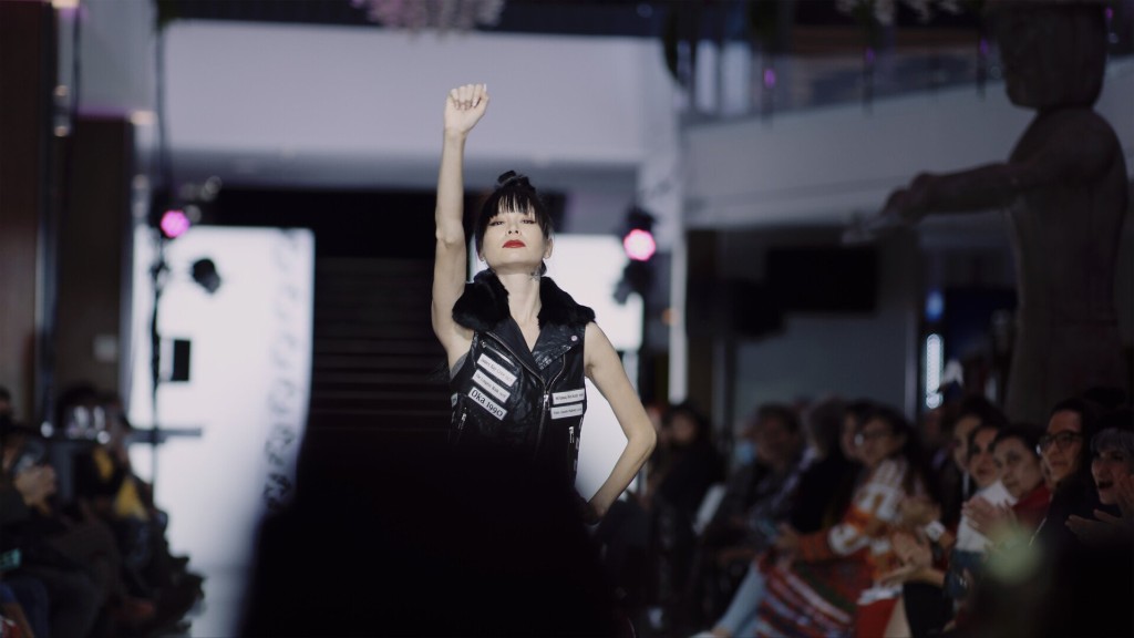 Still image from the film Ancestral Threads, a model walks the runway with one hand on her hip and one fist in the air. Click to follow a link to the film. 