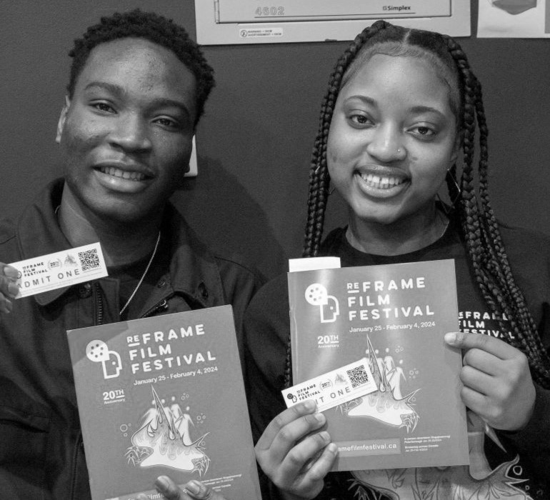 Two people are smiling while holding programs and tickets for the ReFrame Film Festival. Both are standing close together, each holding an 