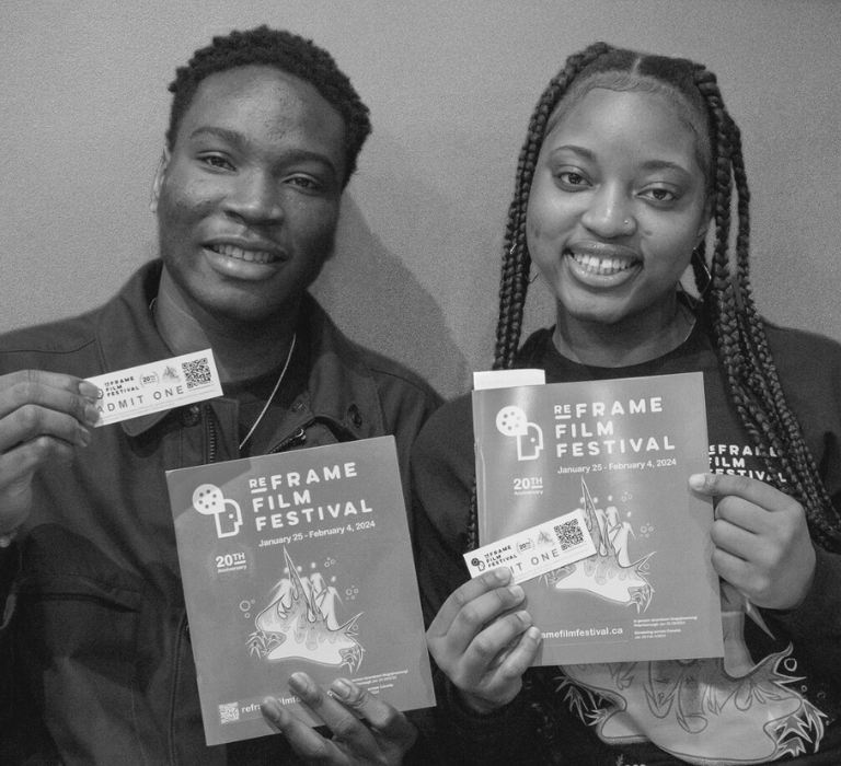 Two ReFrame volunteers hold up programmes and tickets, smiling at the camera.