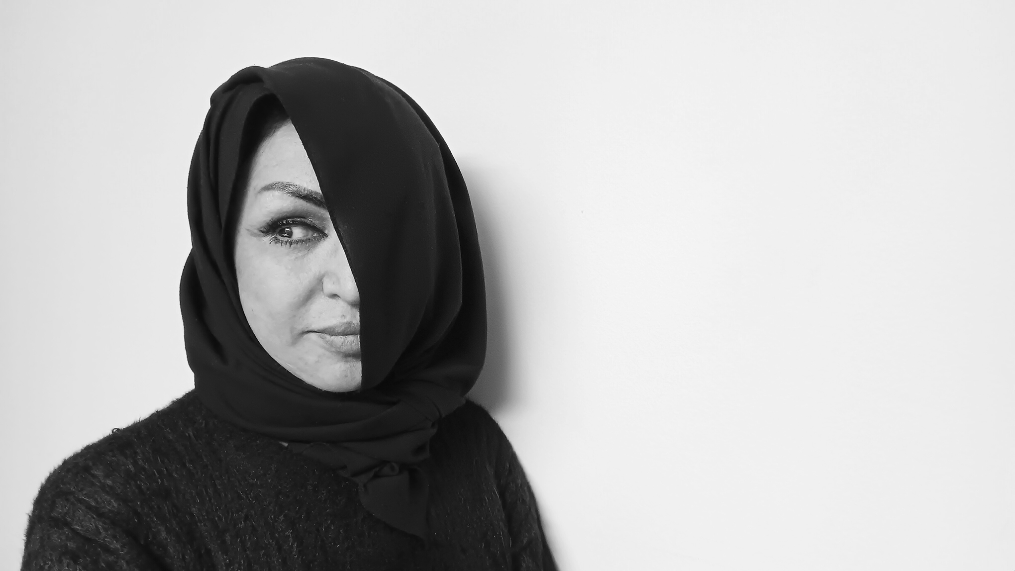 A black and white photo of a woman, from the shoulders up, wearing a headscarf which covers the left side of their face.